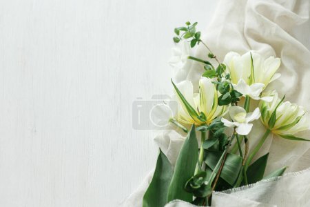 Foto de Feliz Día de las Madres. Hermosos tulipanes blancos y narcisos sobre tela suave sobre mesa de madera rústica plana con espacio para el texto. Elegante ramo de primavera del jardín. Día de las mujeres - Imagen libre de derechos