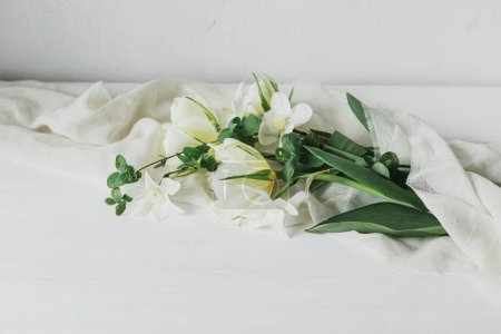 Foto de Hermosos tulipanes blancos y narcisos sobre tela suave sobre mesa de madera rústica. Feliz Día de las Madres. Elegante ramo de primavera simple, bodegón floral. Día de las mujeres. Espacio para texto - Imagen libre de derechos