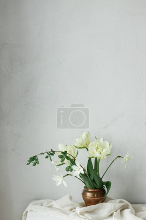 Téléchargez les photos : Bonne fête des mères. Belles tulipes blanches et jonquilles en vase vintage sur table en bois contre mur rustique. Bouquet de printemps simple et élégant, nature morte florale. Journée des femmes. Espace pour le texte - en image libre de droit