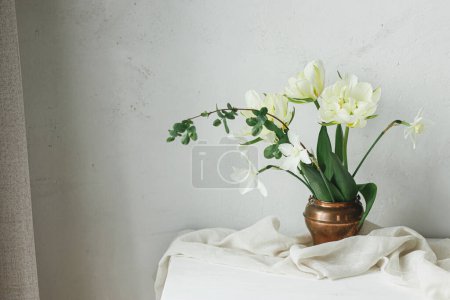 Téléchargez les photos : Bonne fête des mères. Belles tulipes blanches et jonquilles en vase vintage sur table en bois contre mur rustique. Bouquet de printemps simple et élégant, nature morte florale. Journée des femmes. Espace pour le texte - en image libre de droit