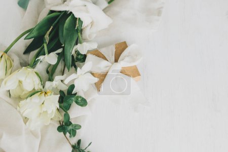 Foto de Hermoso ramo blanco con caja de regalo sobre una mesa de madera rústica. Feliz Día de las Madres. Elegantes tulipanes de primavera y narcisos sobre tela suave y presente. Día de las mujeres. Espacio para texto - Imagen libre de derechos