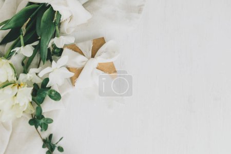 Foto de Feliz Día de las Madres. Hermoso ramo blanco con caja de regalo sobre una mesa de madera rústica. Elegantes tulipanes de primavera y narcisos sobre tela suave y presente. Día de las mujeres. Espacio para texto - Imagen libre de derechos