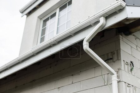 Photo for Rain water drainage system concept. Building with white pipe for rain water, roof, unfinished facade, white windows. Modern new farmhouse building exterior. - Royalty Free Image