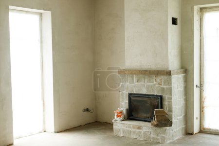 Foto de Chimenea en la sala de estar sin terminar, concepto de renovación del hogar. Chimenea decorativa con piedra natural y repisa de madera. Mejora habitación - Imagen libre de derechos