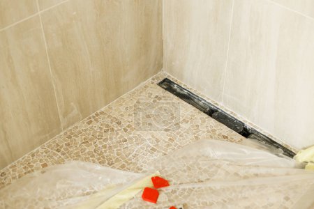 Téléchargez les photos : Drain de douche au sol et mosaïque moderne de tuiles travertin dans la salle de bain inachevée. Construction d'une maison et rénovation de la maison concept. Canalisations de plomberie - en image libre de droit