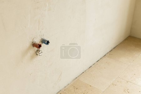 Foto de Tubería de agua en la pared y azulejos de travertino en el suelo en el baño sin terminar. Construcción de la casa y el concepto de renovación del hogar. Tuberías de fontanería - Imagen libre de derechos