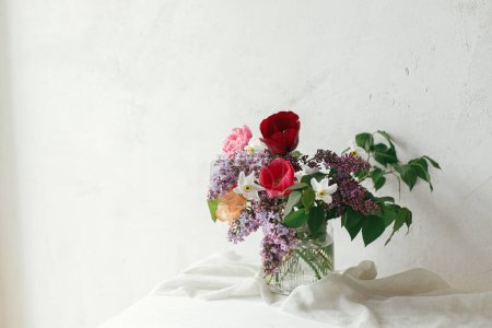 Téléchargez les photos : Bouquet élégant sur table rustique en bois. Bonne fête des mères. Lilas printanier, tulipes, jonquilles agencement sur tissu doux dans une pièce rustique moderne. Joyeuse journée des femmes - en image libre de droit