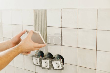 Photo for Worker installing stylish white tiles on wall at electricity socket. Hands laying modern square tile on adhesive close up. Renovation, home improvement - Royalty Free Image