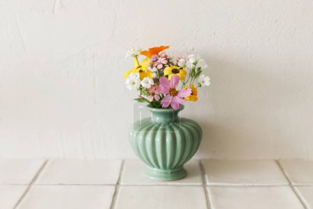 Téléchargez les photos : Élégant bouquet de fleurs sauvages colorées sur une étagère de tuiles sur fond de mur rustique. Belles fleurs d'été dans un vase recueilli du jardin, arrangement floral dans la chambre moderne dans la maison - en image libre de droit