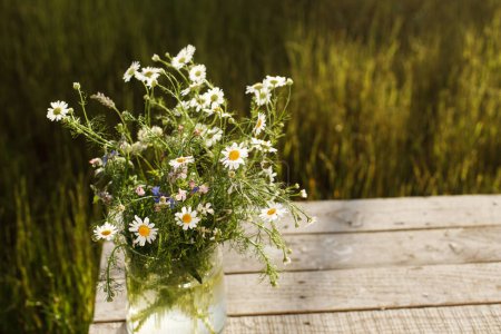 Photo for Beautiful wildflowers bouquet in sunlight on rustic wooden table in garden among grass. Beautiful summer flowers in vase gathered from garden, arrangement in countryside home. Copy space - Royalty Free Image