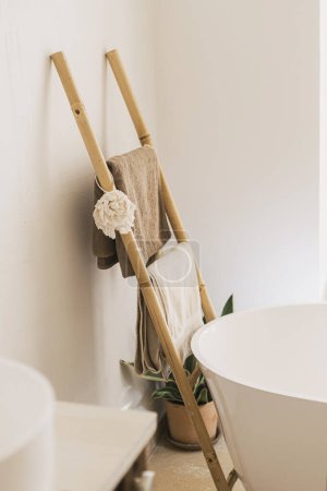 Foto de Elegante diseño de baño boho. Escalera de madera rústica con toallas y paño en la bañera moderna, baño interior moderno. - Imagen libre de derechos