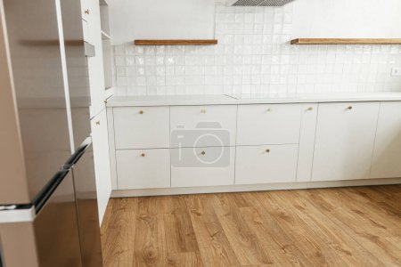 Foto de Moderno diseño de cocina minimalista. Elegantes armarios de cocina blancos con pomos de latón, estantes de madera y electrodomésticos en la nueva casa escandinava. Interior de cocina moderna - Imagen libre de derechos