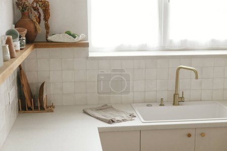 Photo for Modern kitchen interior. Stylish white kitchen cabinets, brass faucet and granite sink, wooden shelves with utensils  in new scandinavian house. Modern minimal kitchen design - Royalty Free Image