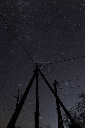 Téléchargez les photos : Ciel nocturne incroyable avec des étoiles et des tours de pouvoir avec des lignes dans la campagne. Beau ciel étoilé et fils électriques - en image libre de droit