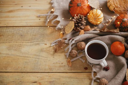 Téléchargez les photos : Autumn flat lay. Warm cup of tea, pumpkins, fall leaves, cozy scarf and lights on rustic wooden table with space for text. Hygge fall banner. Happy Thanksgiving - en image libre de droit