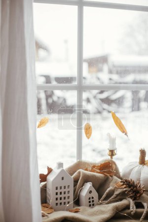 Photo for Cozy Autumn. Stylish pumpkin pillows, fall leaves, candle, lights and cute buildings decoration on brown scarf on windowsill. Autumn hygge, fall home decor. Happy Thanksgiving - Royalty Free Image