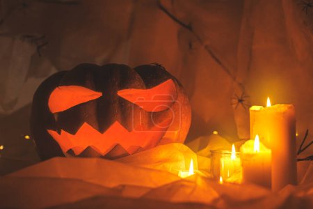 Foto de ¡Feliz Halloween! Jack o linterna calabaza tallada, telaraña, fantasma y luces brillantes en interiores oscuros. Espeluznantes decoraciones de halloween atmosférico con velas en la noche. Truco o trato - Imagen libre de derechos