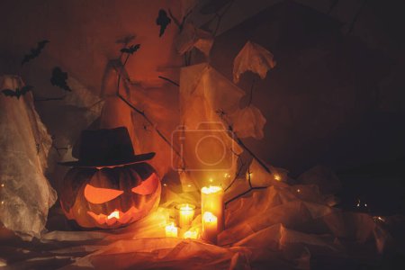 Téléchargez les photos : Joyeux Halloween ! Spooky Jack o lanterne sculptée citrouille, toile d'araignée, fantôme, chauves-souris et la lumière brillante dans l'obscurité. Décorations de fête d'Halloween atmosphériques effrayantes, espace pour le texte. Trick ou traiter - en image libre de droit