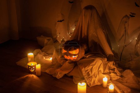 Foto de Fantasma aterrador sosteniendo a Jack o linterna en la oscuridad. Decoraciones de Halloween atmosféricas de miedo y persona vestida de fantasma con calabaza brillante. ¡Feliz Halloween! Truco o trato - Imagen libre de derechos