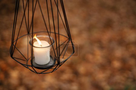 Téléchargez les photos : Lanterne noire minimaliste moderne avec bougie allumée sur fond de feuilles d'automne en forêt. Bonjour Fall ! Lanterne brillante dans les bois d'automne humides. Espace de copie. Heure d'Halloween - en image libre de droit