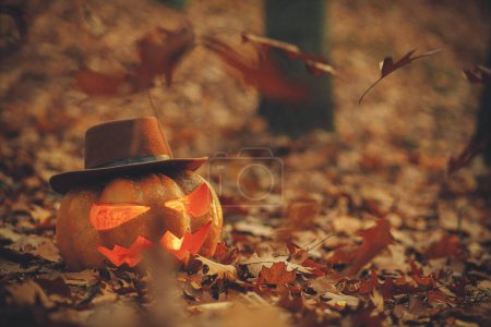 Photo for Happy Halloween! Jack o lantern in hat on autumn leaves in moody dark forest. Spooky atmospheric halloween carved pumpkin in evening fall woods. Trick or treat. Copy space - Royalty Free Image