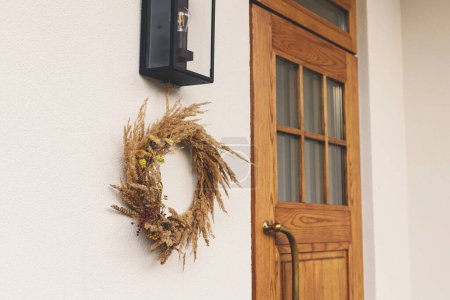 Foto de Corona rústica de otoño colgando en la pared en la entrada de la casa. Elegante decoración otoñal de entrada de casa de campo o porche. Acuerdo de caída - Imagen libre de derechos