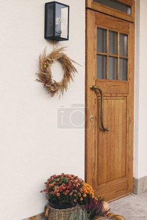 Photo for Autumn rustic wreath, pumpkins and flower pots at wooden front door. Stylish autumnal decor of farmhouse entrance or porch. Fall arrangement - Royalty Free Image
