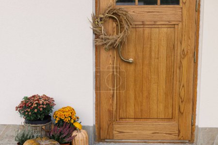 Foto de Corona rústica de otoño, calabazas y macetas en la puerta principal de madera. Elegante decoración otoñal de entrada de casa de campo o porche. Acuerdo de caída - Imagen libre de derechos