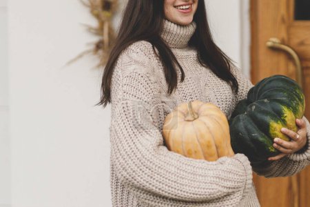 Téléchargez les photos : Femme heureuse en pull tricoté tenant de grandes citrouilles d'automne pour la décoration d'entrée de la maison. Femme élégante décoration ferme porte d'entrée. Arrangement d'automne - en image libre de droit
