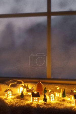 Photo for Atmospheric miniature winter village. Stylish cute little glowing houses and christmas trees on soft snowy blanket in evening room. Christmas hygge background. Happy Holidays! - Royalty Free Image