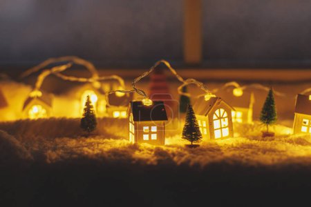 Téléchargez les photos : Confortable village miniature de Noël. Élégantes petites maisons lumineuses et des arbres de Noël sur une couverture de neige molle avec des lumières dans la salle du soir. Village d'hiver atmosphérique nature morte. Joyeux Noël! - en image libre de droit