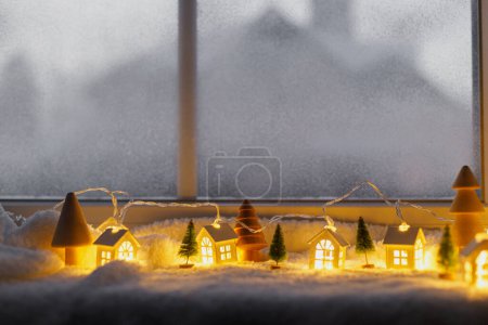 Foto de Acogedor pueblo en miniatura de Navidad. Pequeñas y elegantes casas brillantes y árboles de Navidad en una suave manta de nieve con luces en la sala de la noche. Aldea invernal atmosférica bodegón. Feliz Navidad.! - Imagen libre de derechos