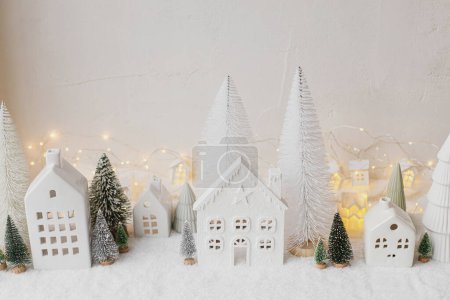 Téléchargez les photos : Village de Noël blanc miniature atmosphérique. Élégantes petites maisons de Noël et des arbres sur la couverture de neige avec des lumières éclatantes. Village d'hiver moderne de Noël, bannière de vacances. Joyeuses fêtes! - en image libre de droit