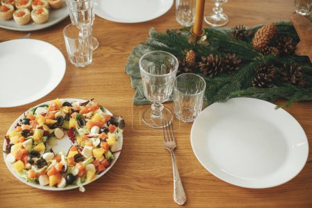 Téléchargez les photos : Table de Noël. Salade moderne avec du saumon comme couronne de Noël, entrées et entrées, verres et couverts sur table en bois avec branches de sapin et cônes de pin. Arrangement et fête de vacances - en image libre de droit