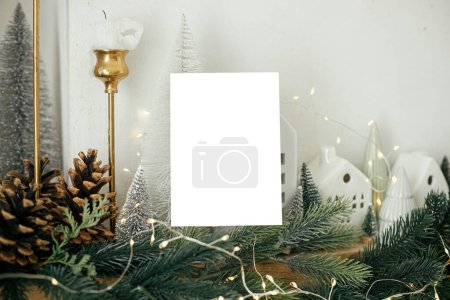 Photo for Christmas card mock up. Empty greeting card on background of stylish  christmas houses, fir branches with golden lights and tree decorations. Space for text. Season greetings template - Royalty Free Image