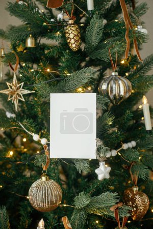 Téléchargez les photos : Carte de Noël maquillée. Carte de vœux vide sur fond d'arbre de Noël décoré élégant avec des lumières dorées. Espace pour le texte. Modèle de salutations saisonnières. Carte postale et ornements vintage - en image libre de droit