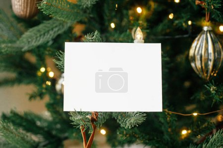 Téléchargez les photos : Carte de vœux vide sur fond d'arbre de Noël décoré élégant avec des lumières dorées. Espace pour le texte. Carte de Noël maquillée. Modèle de salutations saisonnières. Carte postale et ornements vintage - en image libre de droit