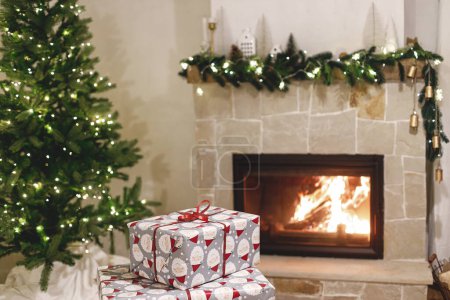 Téléchargez les photos : Cadeaux de Noël enveloppés élégants, arbre de Noël avec des lumières festives et cheminée à combustion confortable. Veille de Noël atmosphérique, temps des fêtes. Joyeux Noël! - en image libre de droit