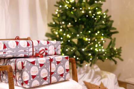 Photo for Merry Christmas! Stylish wrapped christmas gifts on arm chair against christmas tree with festive lights. Atmospheric Christmas eve, holiday time. - Royalty Free Image