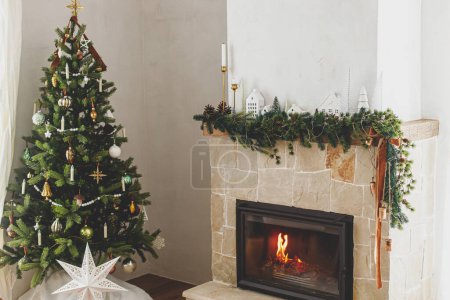 Téléchargez les photos : Élégant arbre de Noël décoré avec des boules vintage et un décor moderne sur cheminée manteau avec cloches et ruban. Salle de séjour scandinave de Noël moderne. Veille de Noël atmosphérique - en image libre de droit