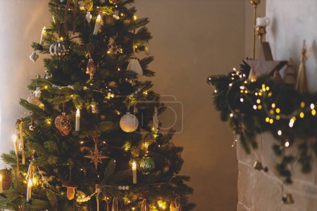 Photo for Atmospheric christmas eve. Stylish illuminated christmas tree with vintage baubles and festive decorated fireplace with golden lights in evening scandinavian room. Merry Christmas! - Royalty Free Image