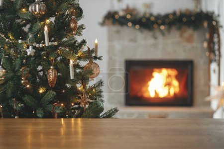 Téléchargez les photos : Modèle de fête de Noël et planche en bois maquettes pour le produit. Table en bois élégant contre l'arbre de Noël avec des lumières et cheminée en feu. Fond de Noël, espace de copie - en image libre de droit