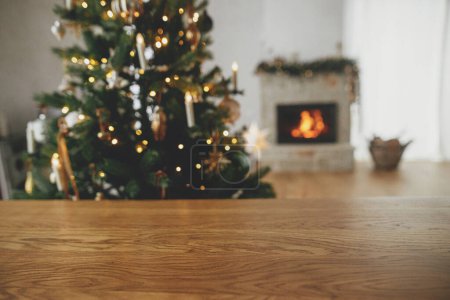 Foto de Plantilla festiva de Navidad y tablero de madera se burlan de producto. Elegante mesa de madera contra el árbol de Navidad con luces y chimenea. Fondo de Navidad, espacio de copia - Imagen libre de derechos