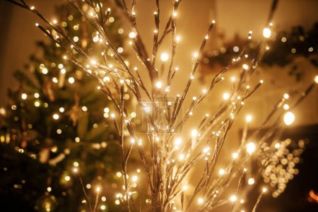 Photo for Stylish christmas illuminated tree on background of golden lights bokeh, decorated tree and burning fireplace in evening room. Atmospheric magical christmas eve at fireplace. - Royalty Free Image