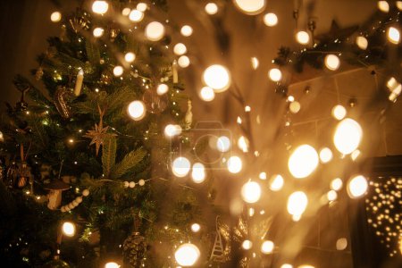 Foto de Nochebuena mágica atmosférica en la chimenea. Elegante árbol iluminado de Navidad en el fondo de luces doradas bokeh, árbol decorado y chimenea en la sala de noche. Feliz Navidad.! - Imagen libre de derechos