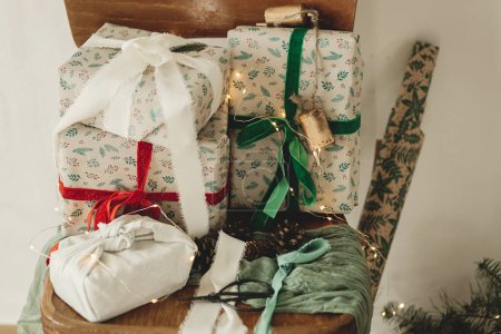 Foto de Feliz Navidad y Felices Fiestas! Elegantes regalos de Navidad envueltos con cintas en una vieja silla de madera, papel festivo y ramas de abeto en la habitación rural. Regalos ecológicos - Imagen libre de derechos