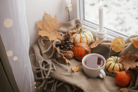 Photo for Autumn hygge. Warm cup of tea, pumpkins, fall leaves, candle, lights bokeh on cozy scarf on windowsill. Happy Thanksgiving. Cozy Autumn, fall home decor - Royalty Free Image