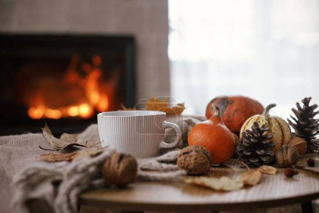 Téléchargez les photos : Warm cup of tea, pumpkins, autumn leaves, cozy scarf on rustic wooden table on background of burning fireplace. Hygge fall home, rural banner. Autumn still life. Happy Thanksgiving - en image libre de droit