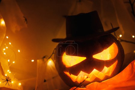 Foto de Spooky Jack o linterna calabaza tallada, telaraña, fantasma, murciélagos y luz brillante en la oscuridad. Espeluznantes decoraciones atmosféricas fiesta de halloween, espacio para el texto. ¡Feliz Halloween! Truco o trato - Imagen libre de derechos