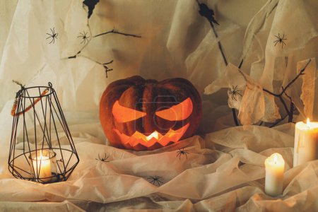 Foto de ¡Feliz Halloween! Jack o linterna calabaza tallada, telaraña, fantasma, murciélagos y velas brillantes en la noche. Espeluznantes decoraciones de halloween atmosférico con luces en interiores. Truco o trato - Imagen libre de derechos